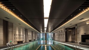A modern indoor swimming pool with a central walkway, surrounded by walls with recessed lighting and a skylight. - Steigenberger Icons Guizhou Xiaoqikong (Qiannan)