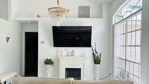 A modern living room with a large sofa, a flat-screen TV, a fireplace, and a large window. - Cozy 3-bedroom house in tranquil Port St. Lucie with AC (Port St. Lucie)