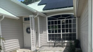 A house with a front porch, a large window, a door with a wreath, and a bench. - Cozy 3-bedroom house in tranquil Port St. Lucie with AC (Port St. Lucie)