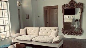 A modern living room with a sofa, ottoman, and a large mirror. - Cozy 3-bedroom house in tranquil Port St. Lucie with AC (Port St. Lucie)