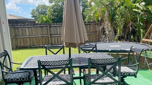 A patio with a table and chairs, surrounded by a wooden fence and greenery. - Cozy 3-bedroom house in tranquil Port St. Lucie with AC (Port St. Lucie)