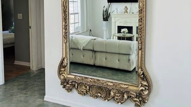 A large ornate mirror with a gold frame, mounted on a white wall in a room with a grey tiled floor. - Cozy 3-bedroom house in tranquil Port St. Lucie with AC (Port St. Lucie)