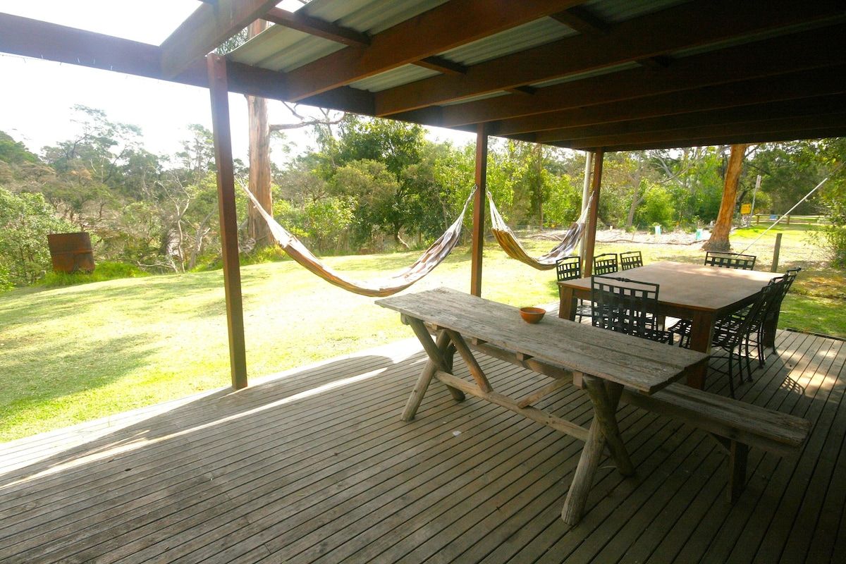 An outdoor wooden deck with a picnic table and chairs, surrounded by greenery.