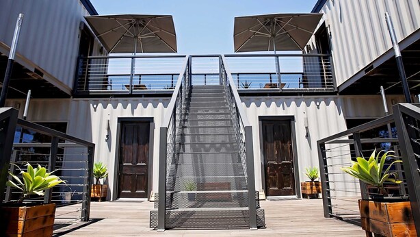 A modern building with a central staircase, outdoor seating, and potted plants.