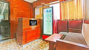 A hotel room with a wooden reception desk, a refrigerator, a bed with a patterned headboard, and a tiled floor. - The Prince Inn (Gurugram)