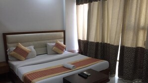 A double bed with a wooden frame, two pillows, a blanket, and a remote control on a small table beside it. - The Prince Inn (Gurugram)