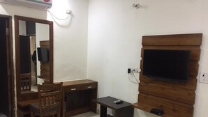 A room with a wooden desk, a chair, a television mounted on the wall, and a small table. - The Prince Inn (Gurugram)