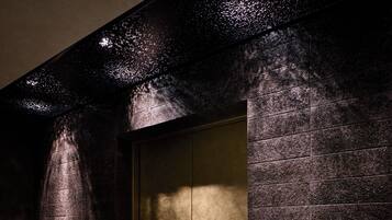 A textured wall with a recessed panel, possibly a door or window, and a corner with a dark, reflective surface.