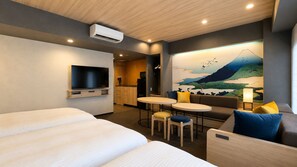 A hotel room with a bed, a TV, a dining area with tables and chairs, a sofa, and a painting of a mountain landscape.