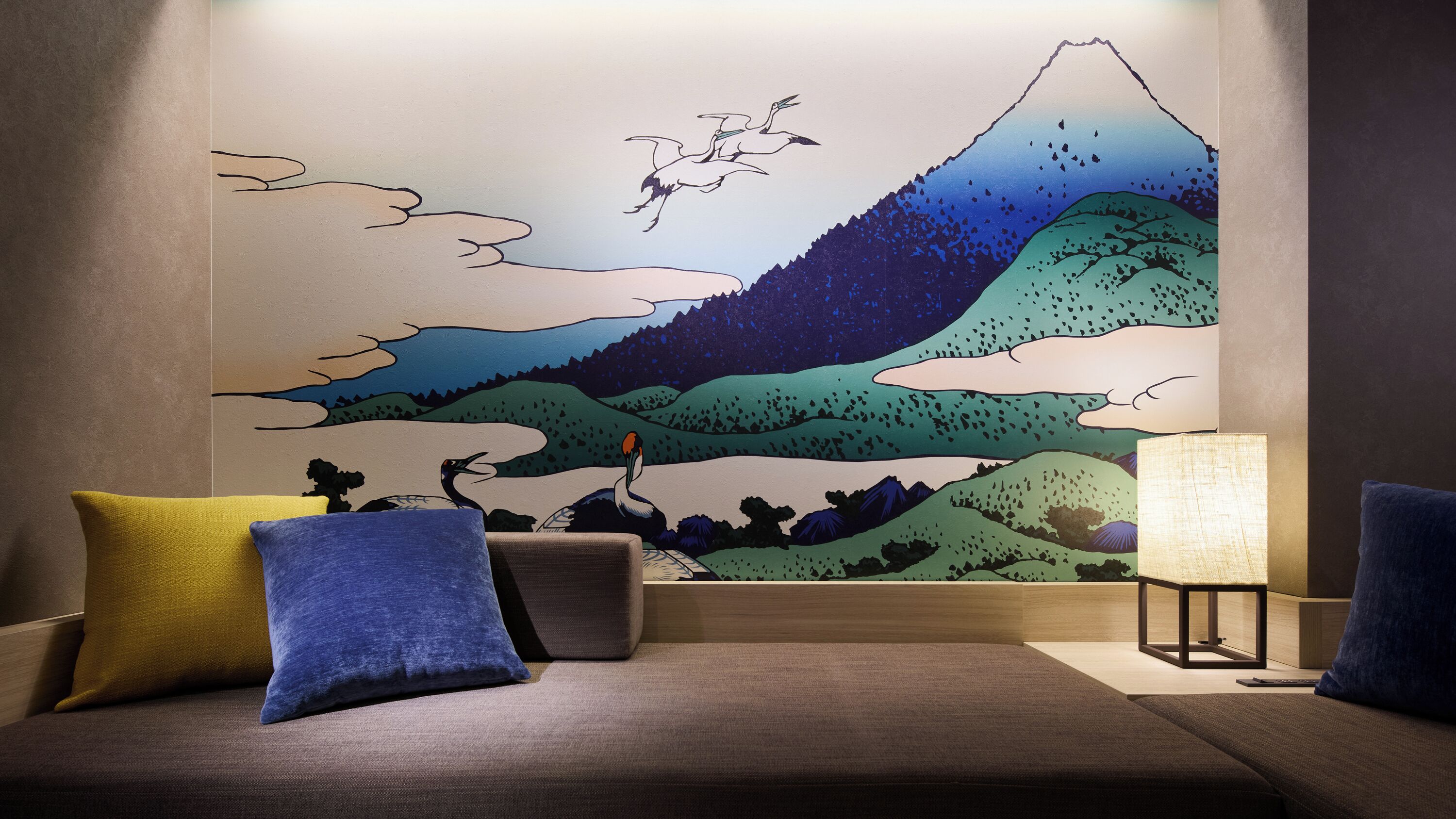 A modern living room with a large wall mural, a sofa with cushions, and a side table with a lamp.