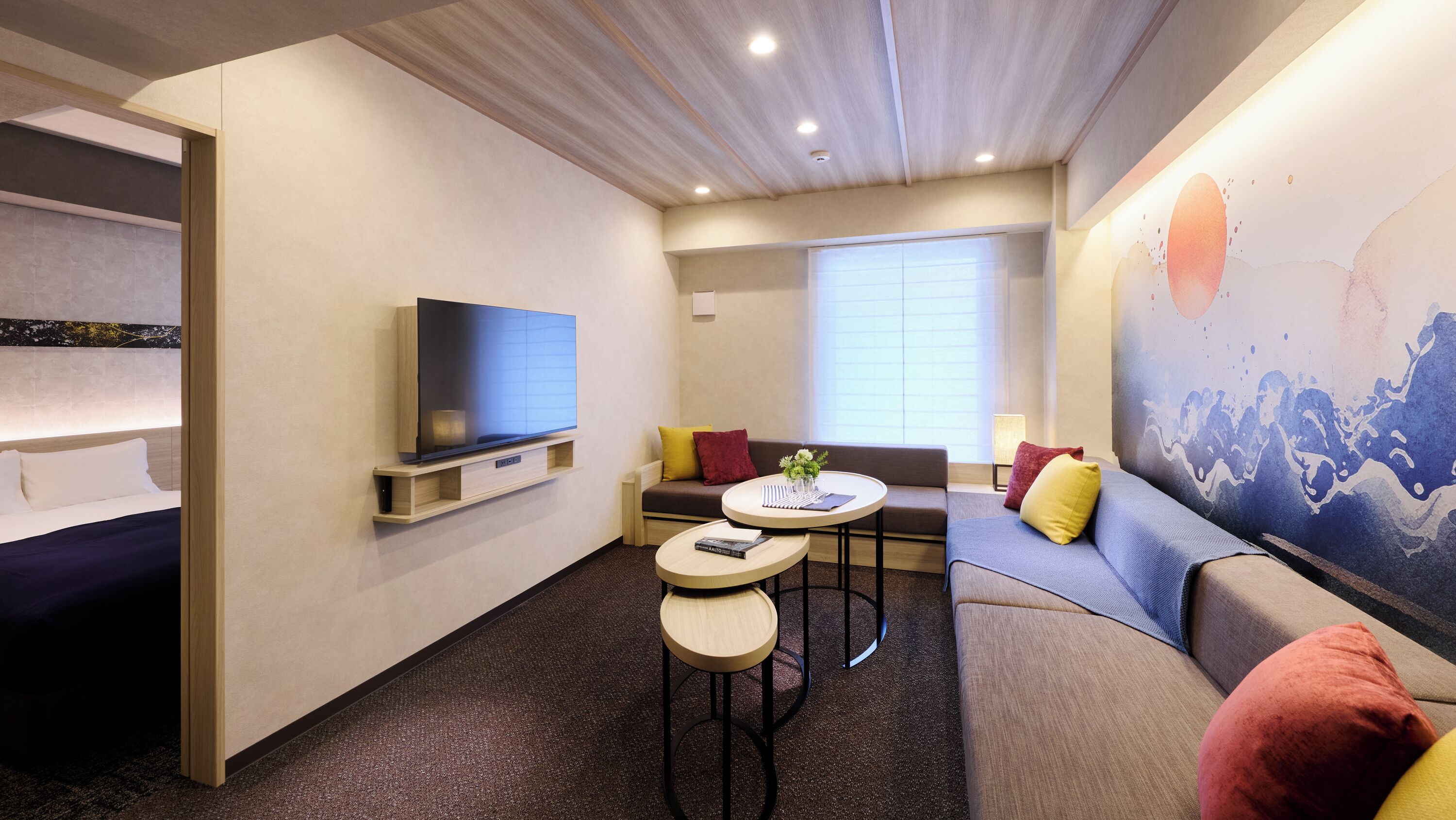 Een moderne hotelkamer met een flatscreen-tv, een bank, een klein tafeltje en een schilderij aan de muur.
