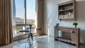 A room with a large window, a wooden console table with plants, a small round table, and two chairs. - ELIVAAS White House 7BHK Villa  (Igatpuri)