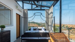 A modern bedroom with a glass ceiling, a bed, a wooden bench, and a view of a hilly landscape. - ELIVAAS White House 7BHK Villa  (Igatpuri)
