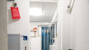 A hallway with a white wall, a red fire extinguisher, a grey cabinet, and a black chair.