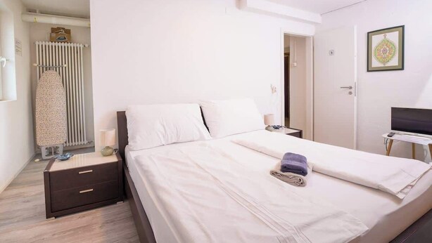 A bedroom with a bed, bedside tables, a radiator, and a desk with a chair.
