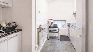 A narrow kitchen with white cabinets, a black countertop, and a small window.