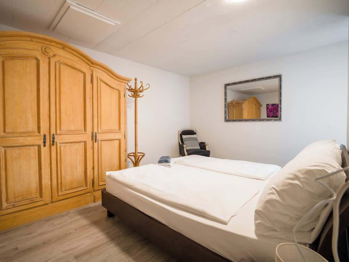 A bedroom with a bed, a wardrobe, a mirror, and a chair.