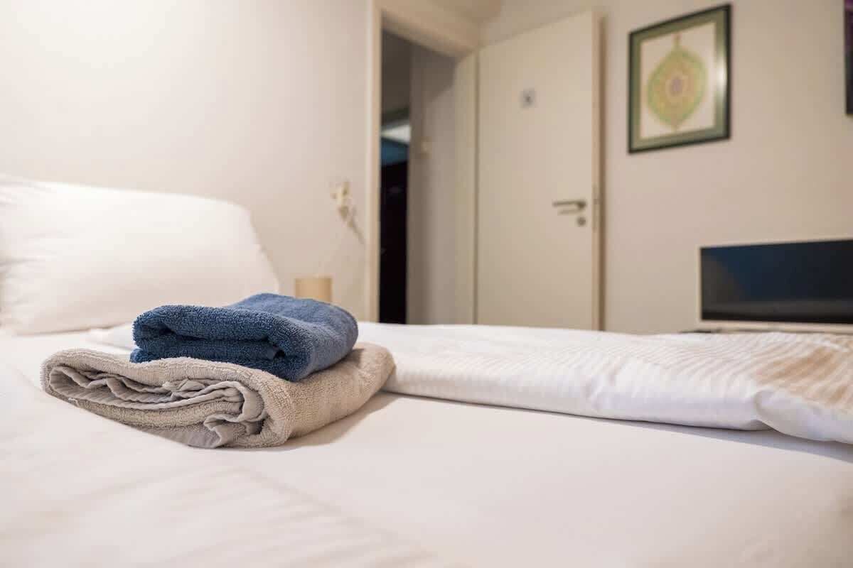 A hotel room with a bed, a folded towel, a television, and a door.