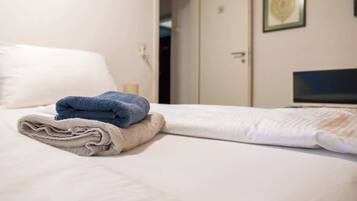 A hotel room with a bed, a folded towel, a television, and a door.