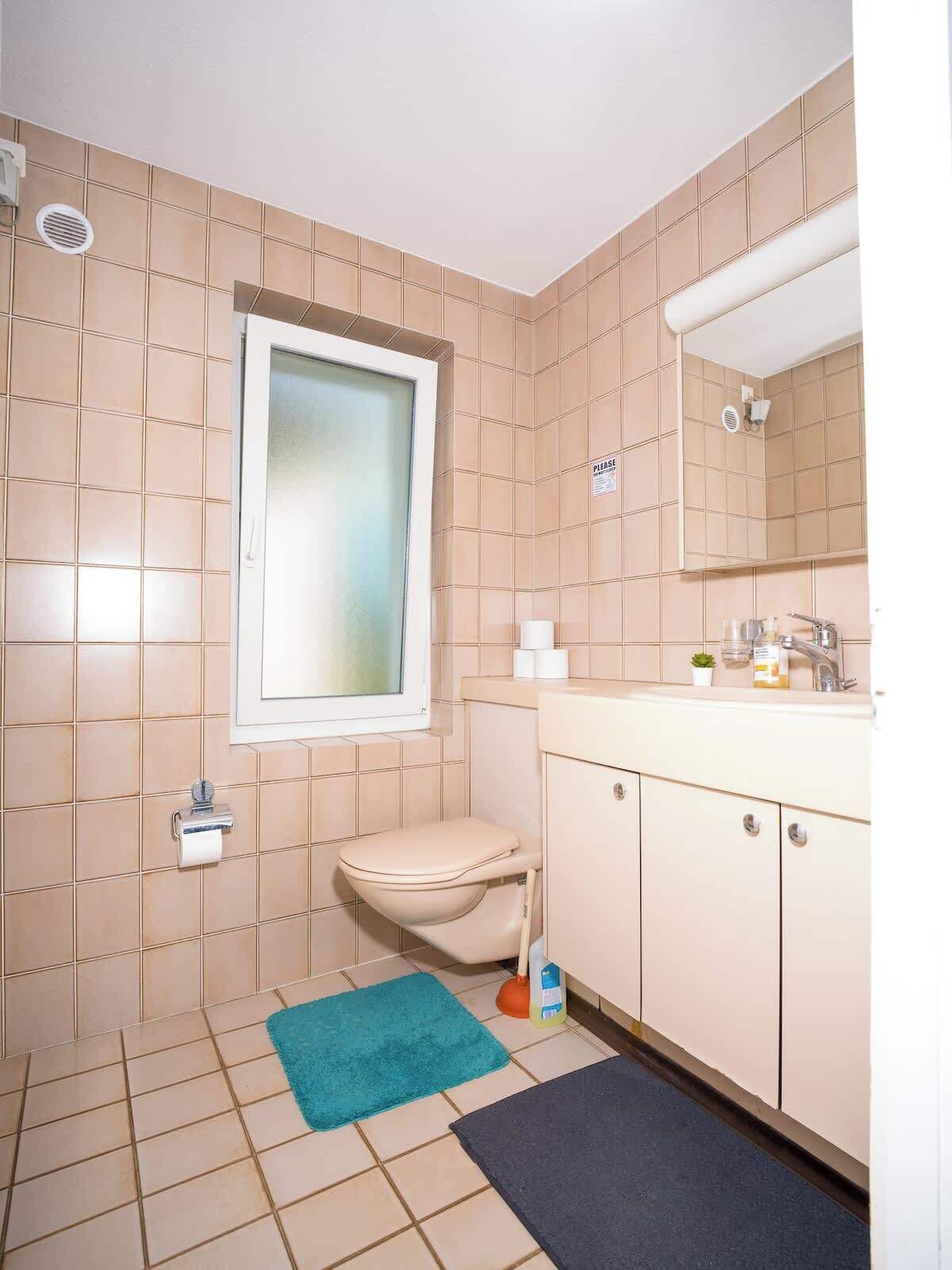 Une petite salle de bain avec des toilettes, un lavabo, un miroir et une fenêtre.