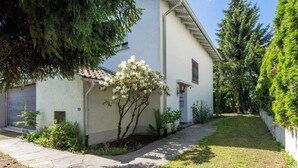 A white building with a tiled roof, a small garden with white flowering plants, and a paved walkway.
