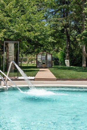 Una piscina con fuente, rodeada de abundante vegetación y una pequeña construcción.