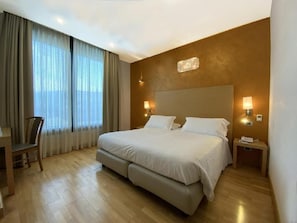 A hotel room with a large bed, a desk, and a chair.