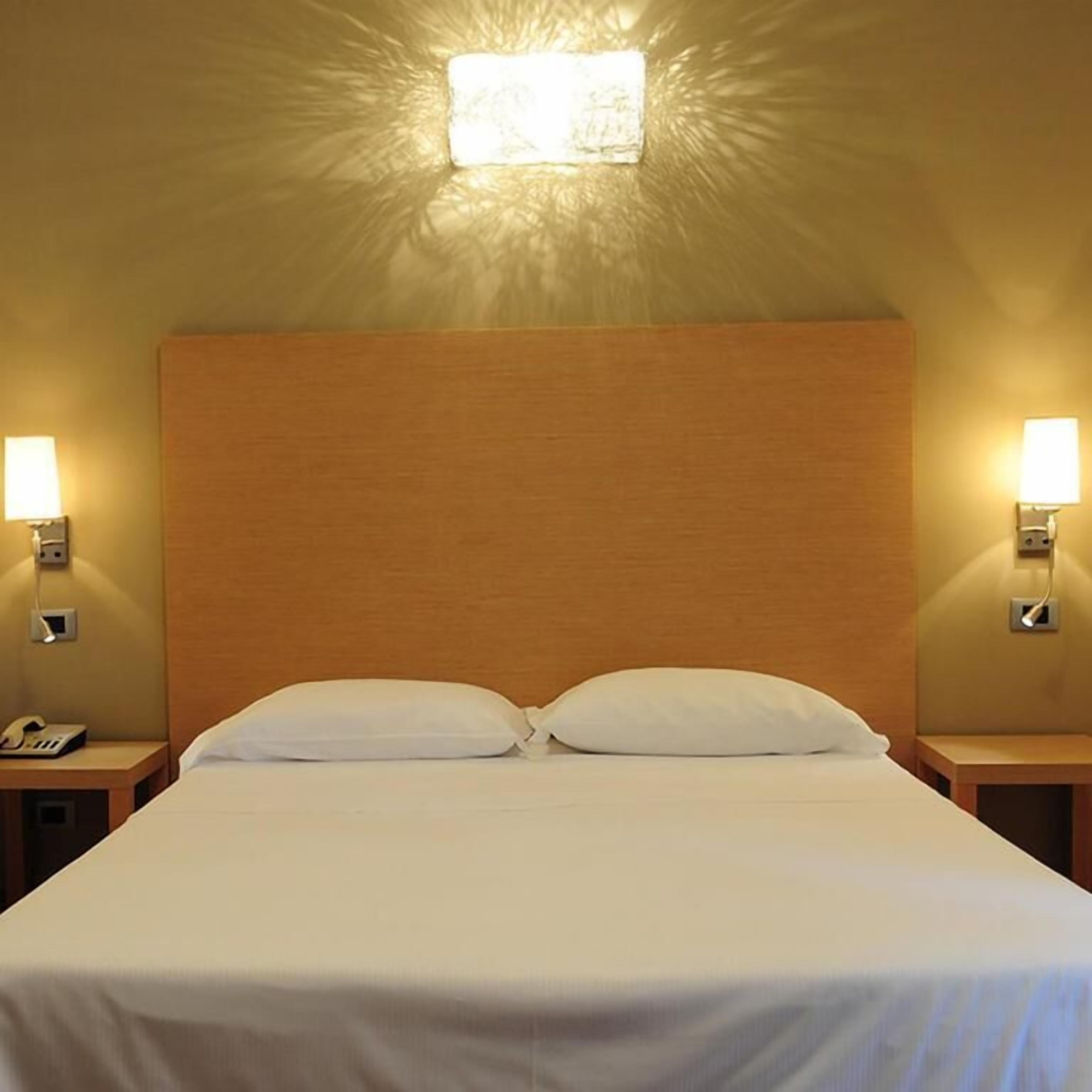 A hotel room with a large bed, two bedside lamps, and a wall-mounted light.