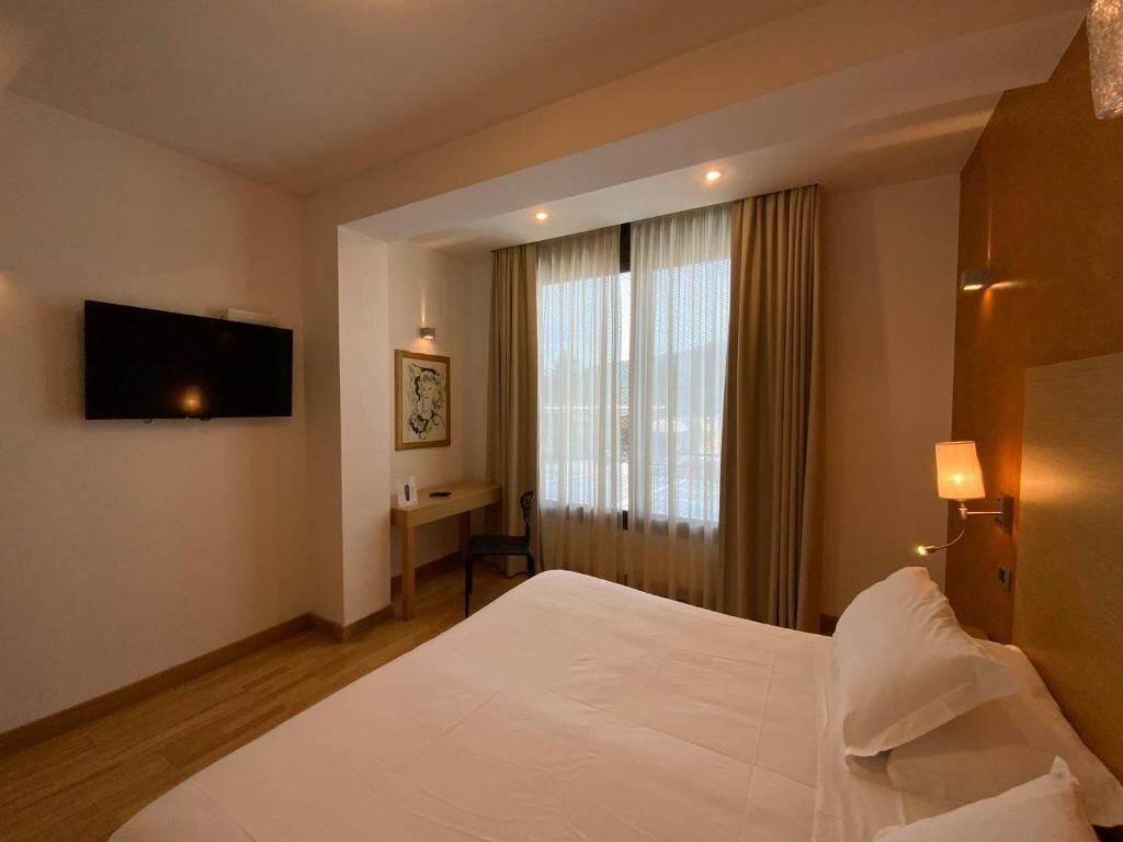 A hotel room with a bed, a desk, a chair, a television, and a window with curtains.