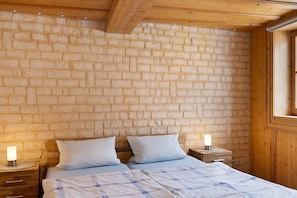 A bedroom with a brick wall, wooden ceiling beams, two beds with white bedding, bedside lamps, and a window. - Apartment 'Stadthaus' with Private Terrace, Balcony and Wi-Fi (Mellrichstadt)