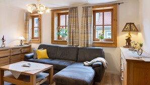 A living room with a sofa, a table, a lamp, and a window with curtains. - Apartment 'Stadthaus' with Private Terrace, Balcony and Wi-Fi (Mellrichstadt)