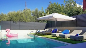 Zwembad met ligbedden en een parasol, omringd door een hek en begroeiing.