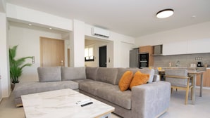 Een moderne woonkamer met een hoekbank, een marmeren salontafel en een keuken met houten kasten en een eettafel.