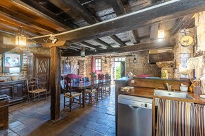 Een rustiek interieur met zichtbare houten balken, stenen muren, een houten eettafel met stoelen, een bar en een Bosch vaatwasser.