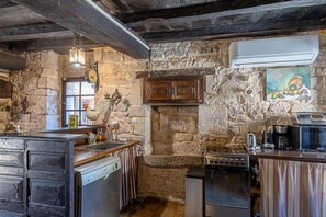 Una cocina rústica con paredes de piedra, techo de madera, estufa empotrada, lavavajillas y cafetera.