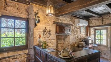 A rustic kitchen with stone walls, wooden beams, a large window, and a rustic wooden table.