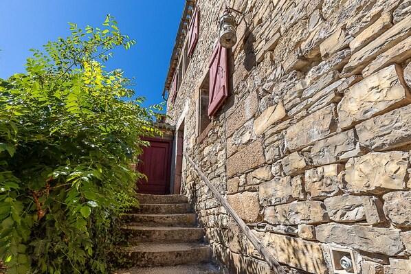 A stone building with a red door and a wooden staircase leading to a red door. - Gîte “Du Château De Vindrac” with Private Pool, Wi-Fi, and Air Conditioning (Milhars)