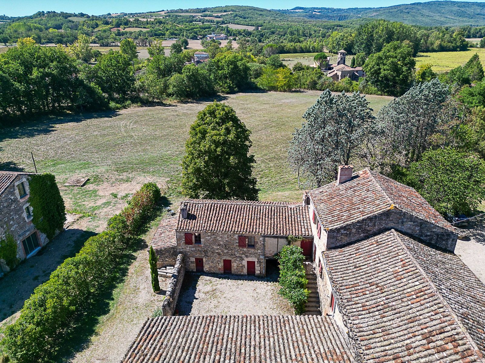 A rural landscape with stone buildings, a clear sky, and rolling hills in the distance.