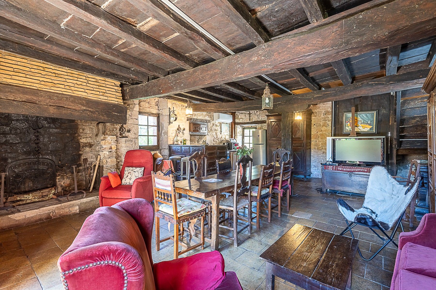 A rustic interior with exposed wooden beams, a stone fireplace, and a dining area with wooden furniture.
