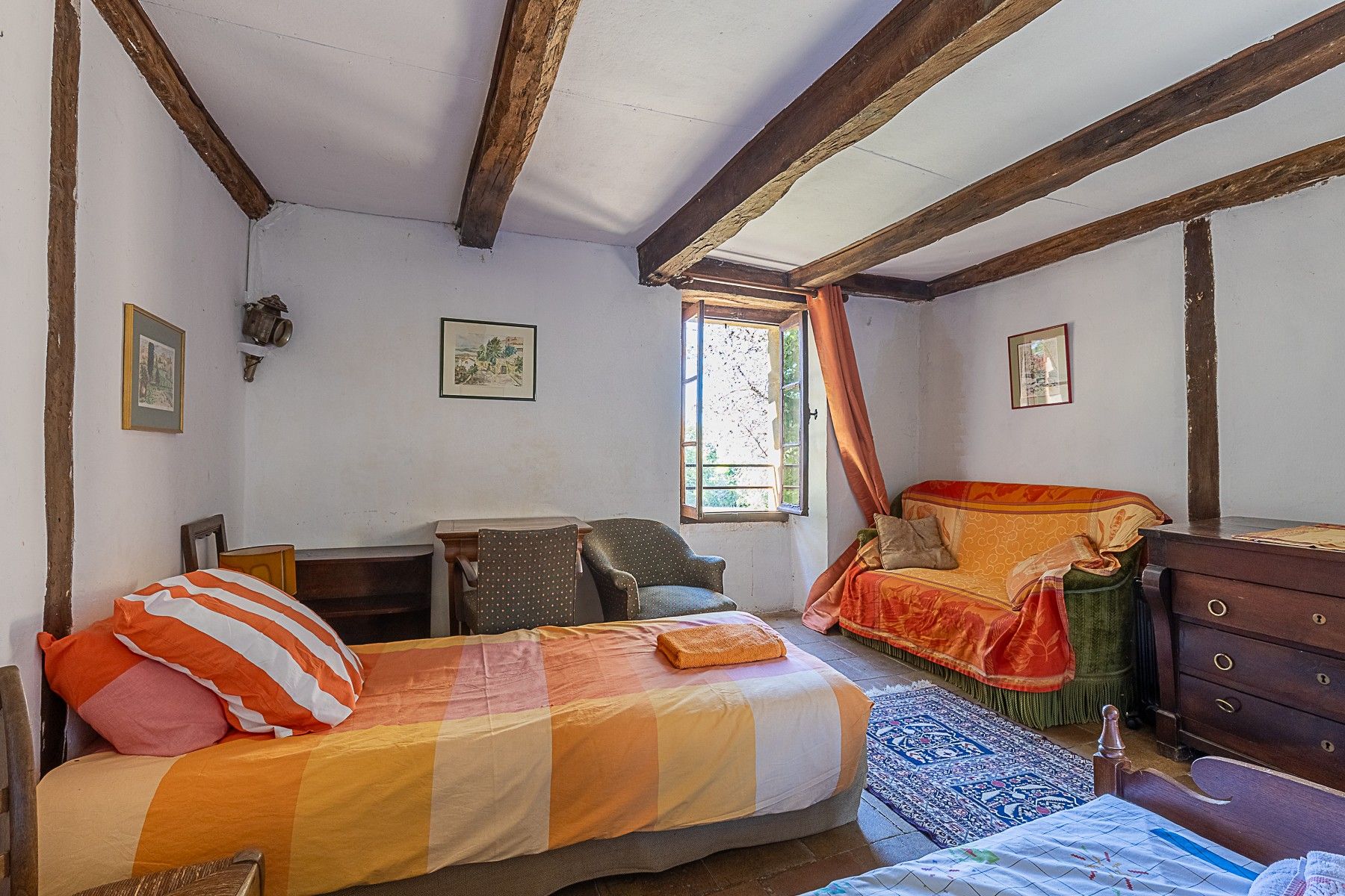 Ein Zimmer mit einem Bett, einem Sessel, einer Kommode und einem Fenster mit Vorhängen.