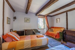 Ein Zimmer mit einem Bett, einem Sessel, einer Kommode und einem Fenster mit Vorhängen.