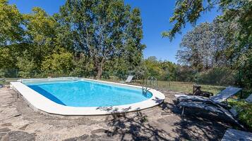 Piscina con borde de baldosas, rodeada de árboles y una valla.