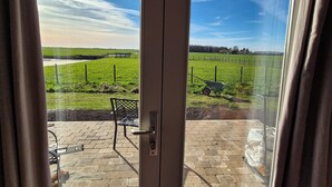A view through a door to a patio with a bench, a wheelbarrow, and a brick floor.