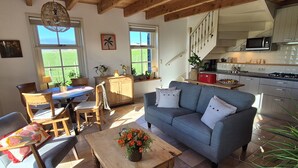 A cozy living room with a sofa, chairs, a wooden coffee table, and a kitchen in the background.