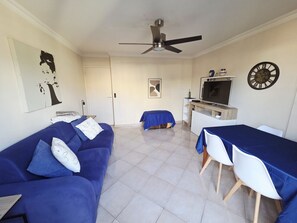 Un salon comprenant un canapé, une table à manger, un téléviseur et un ventilateur de plafond.