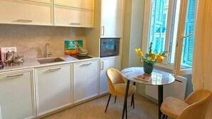 A compact kitchen with white cabinets, a sink, an oven, and a dining area with two chairs and a table. - Mediterranean Dream - Carré d'Or (Nice)