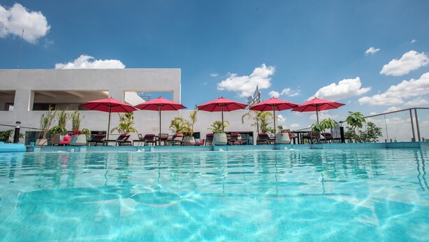 A swimming pool with clear water, surrounded by lounge chairs and red umbrellas, with a modern building in the background. - Modern 2 Bedroom Westlands Nairobi,  with AC, Rooftop Pool, Gym, Squash Court (Nairobi)