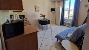 A compact room with a kitchenette, a dining table with chairs, a bed, and a window with curtains. - Le Centrale - Place Massena (Nice)