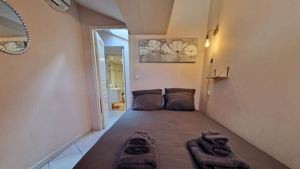 A bedroom with a bed, pillows, a wall-mounted light, and a door leading to a bathroom. - Le Centrale - Place Massena (Nice)
