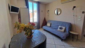 A room with a sofa, a small table with a plant, a TV, and an air conditioner. - Le Centrale - Place Massena (Nice)